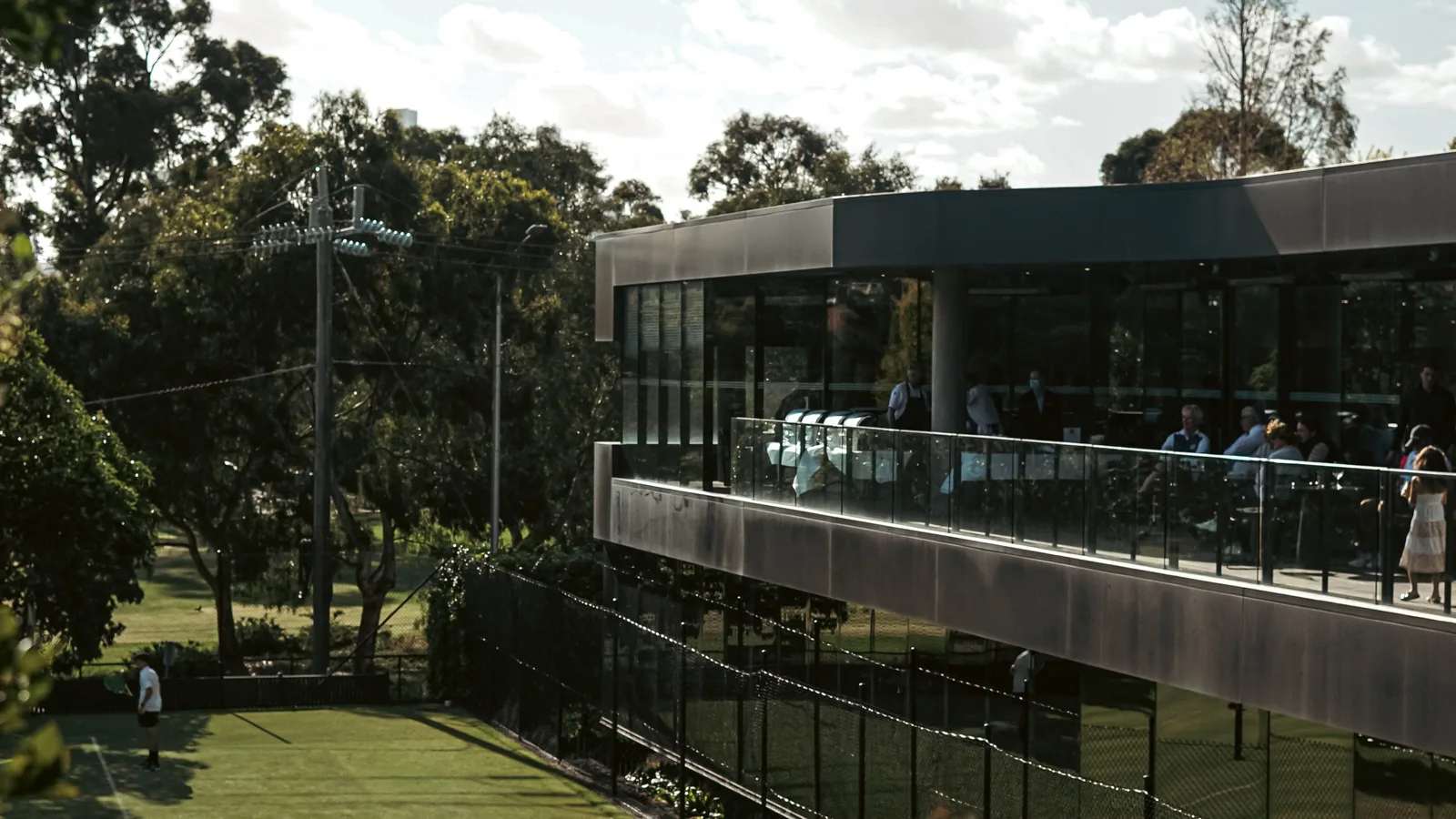 A modern clubhouse terrace overlooking a manicured grass tennis court, illustrating the upscale private-club setting EVC brings its instruction to