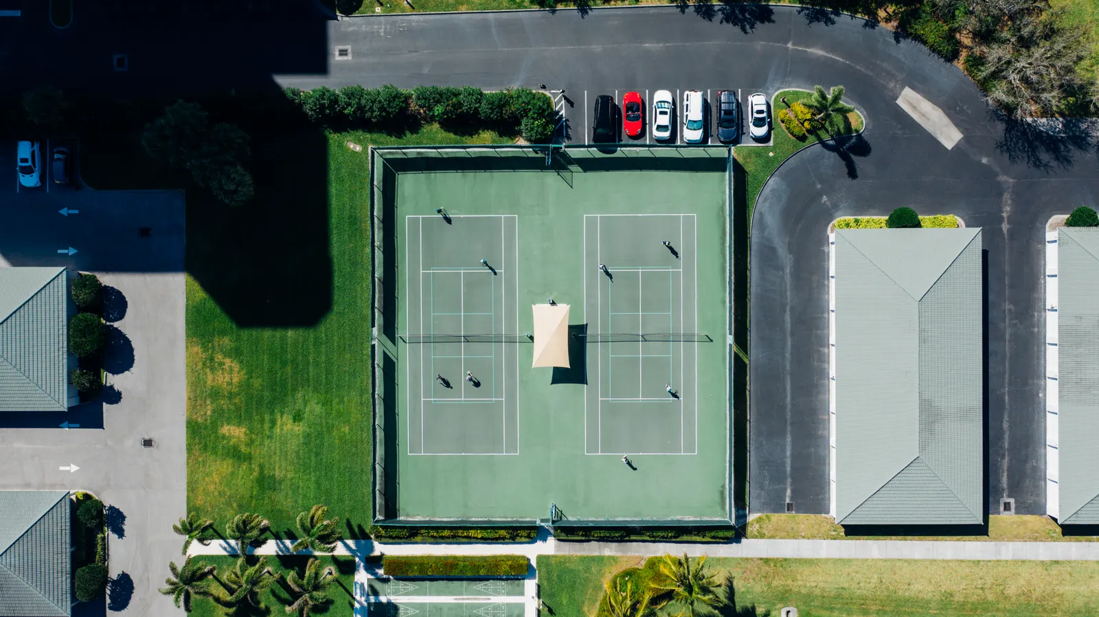 Aerial view of a residential community's tennis courts with residents playing, illustrating the kind of amenity EVC brings to Miami HOA and condominium communities