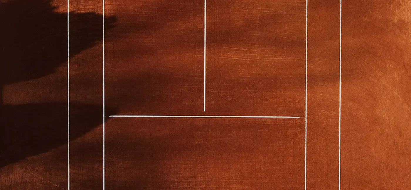 Aerial view of a manicured clay tennis court with crisp white lines