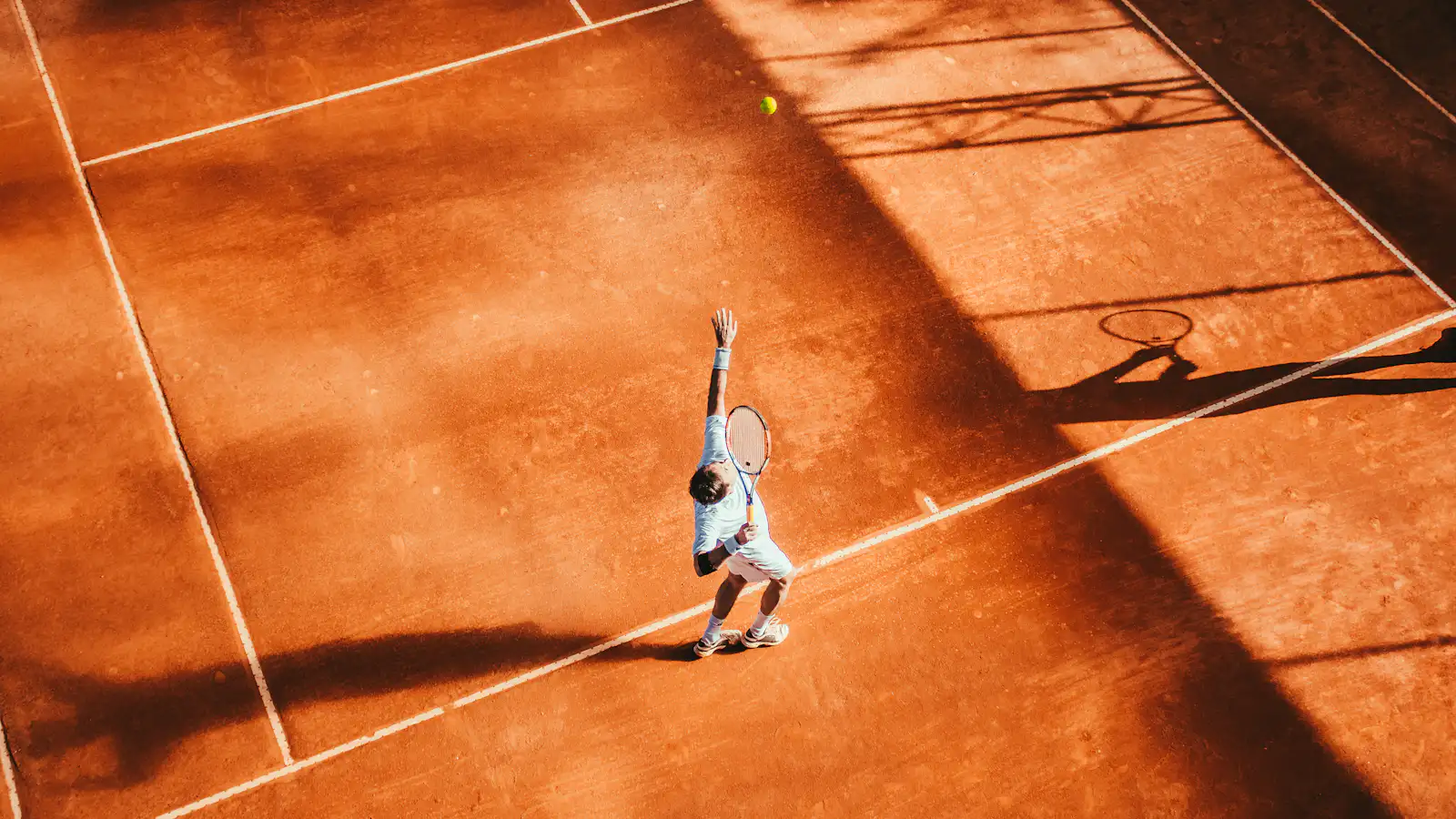 An adult player serving on a sunlit premium clay court, illustrating the guest tennis experience EVC arranges for Miami hotels