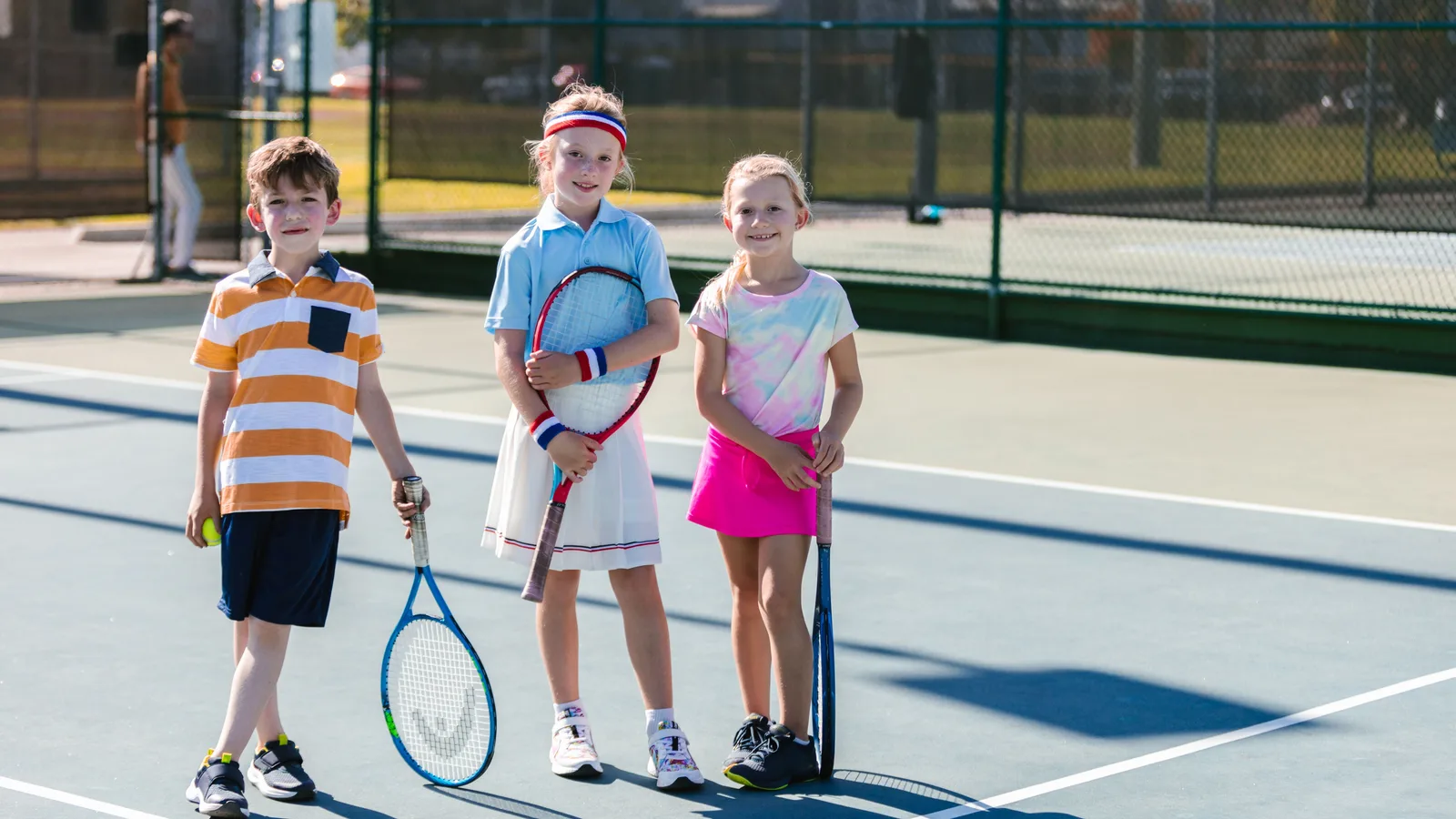 Three diverse youth players holding tennis rackets on an outdoor court, illustrating the organized youth and community tennis programming EVC brings to companies, nonprofits and community organizations