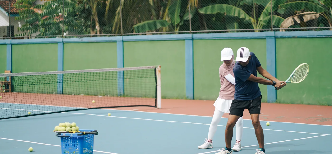 A tennis coach guiding a player's racket technique during an organized lesson