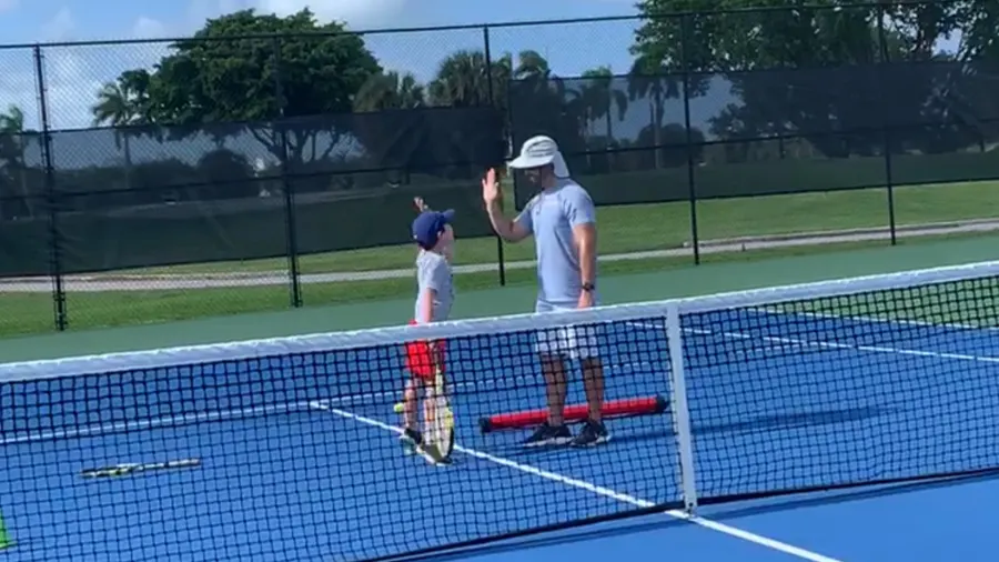 Coach high-fiving young player at net